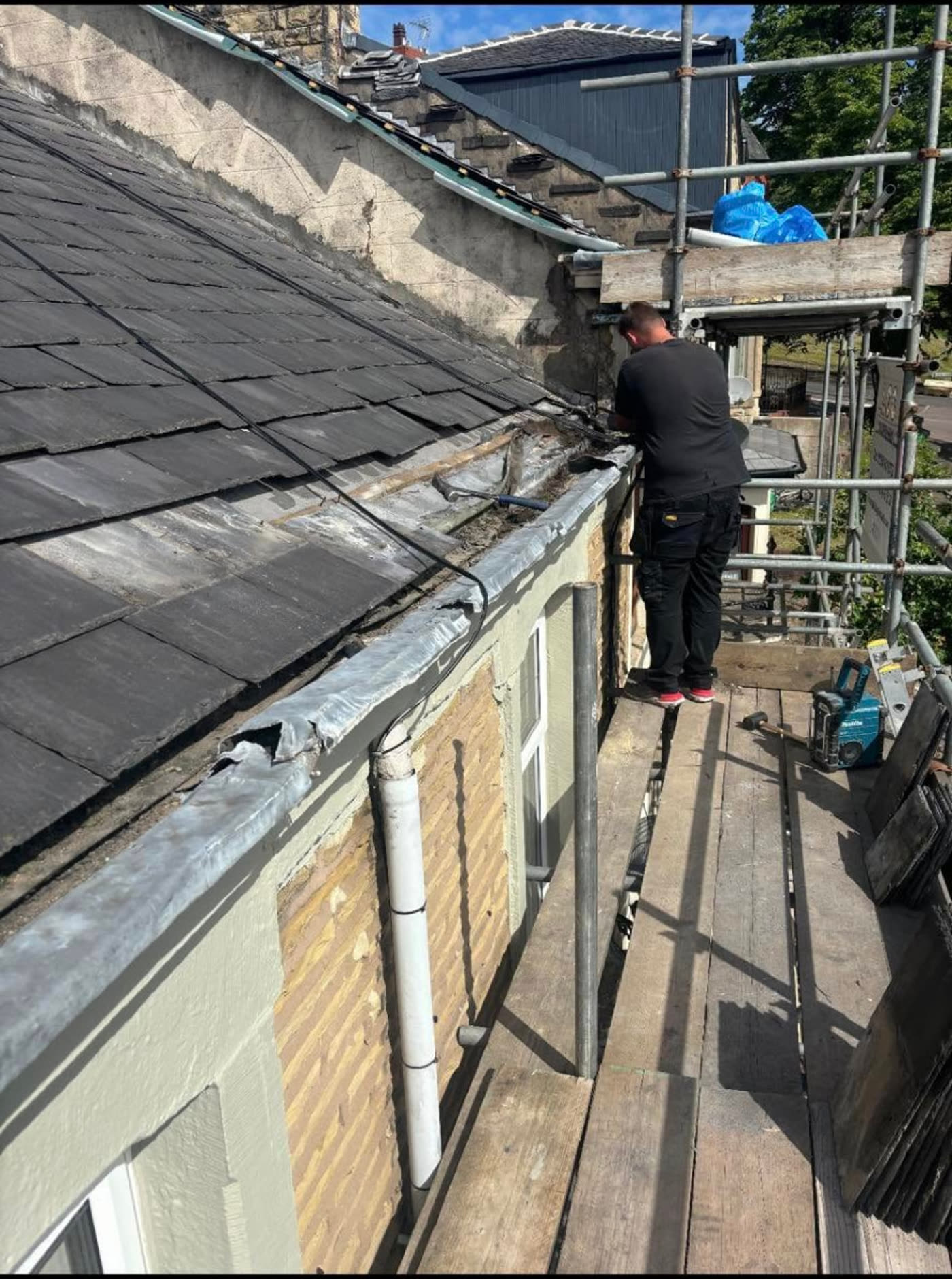 MB Roofline & Joinery tradesman working from scaffolding on a slate roof edge, renewing lead flashing and guttering