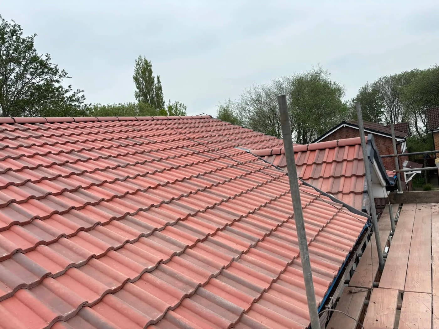 Completed red interlocking tiled roof with a mechanically fixed ridge, viewed from the scaffold